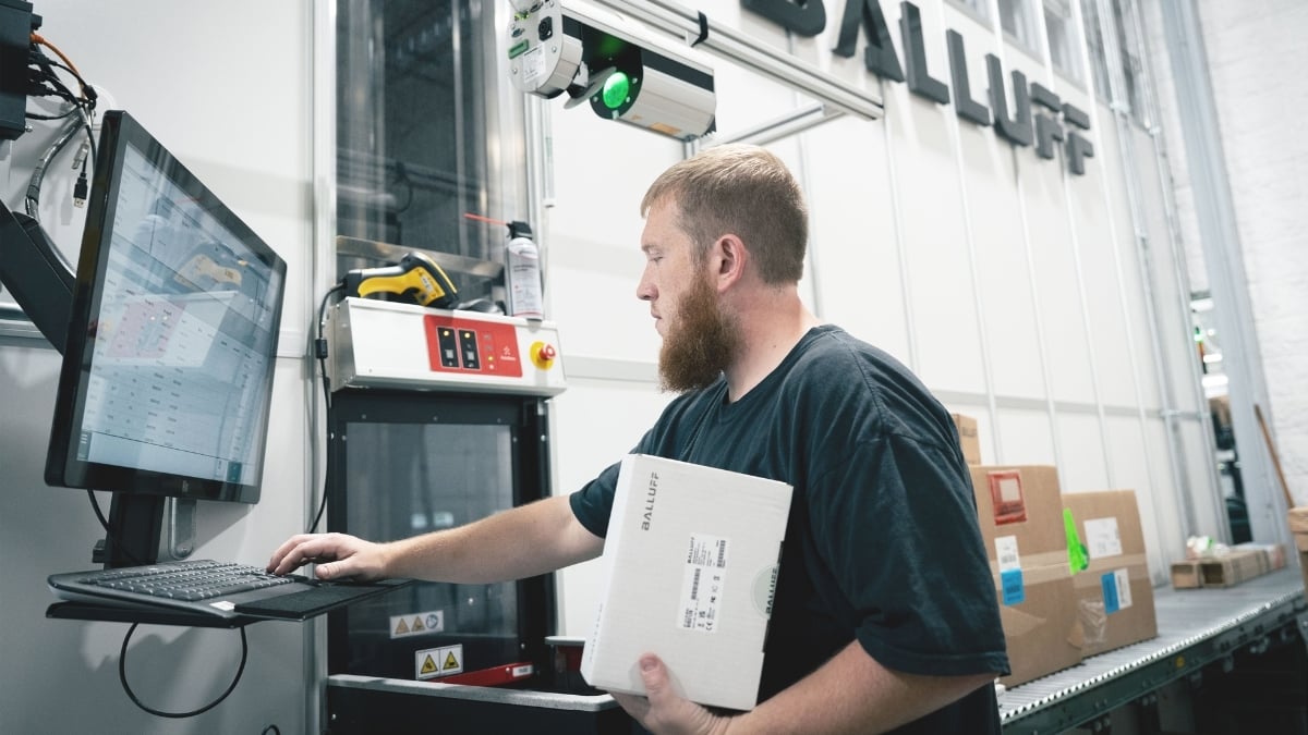 Man picking boxed items out of AutoStore system while working on the computer