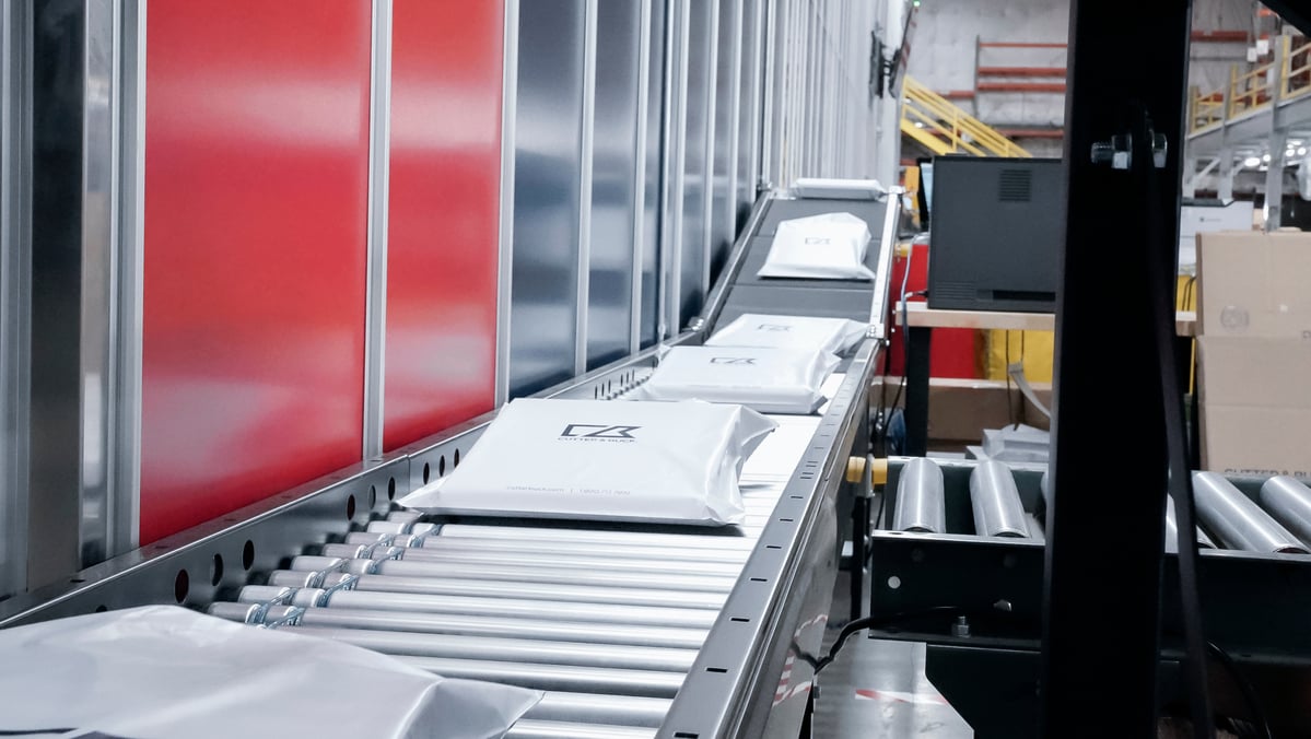 Packages moving down warehouse conveyor belt next to AutoStore system