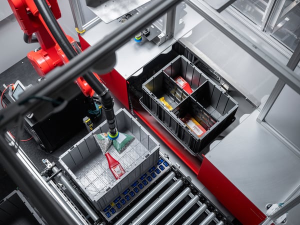 A red robotic arm placing inventory from a bin into an outbound tote on a conveyor