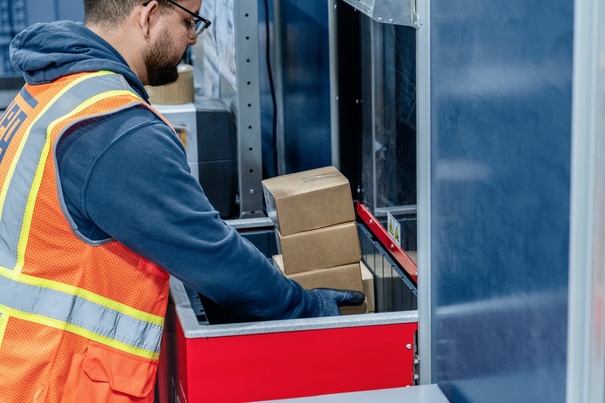 Warehouse worker in safety vest retrieving spare parts from AutoStore