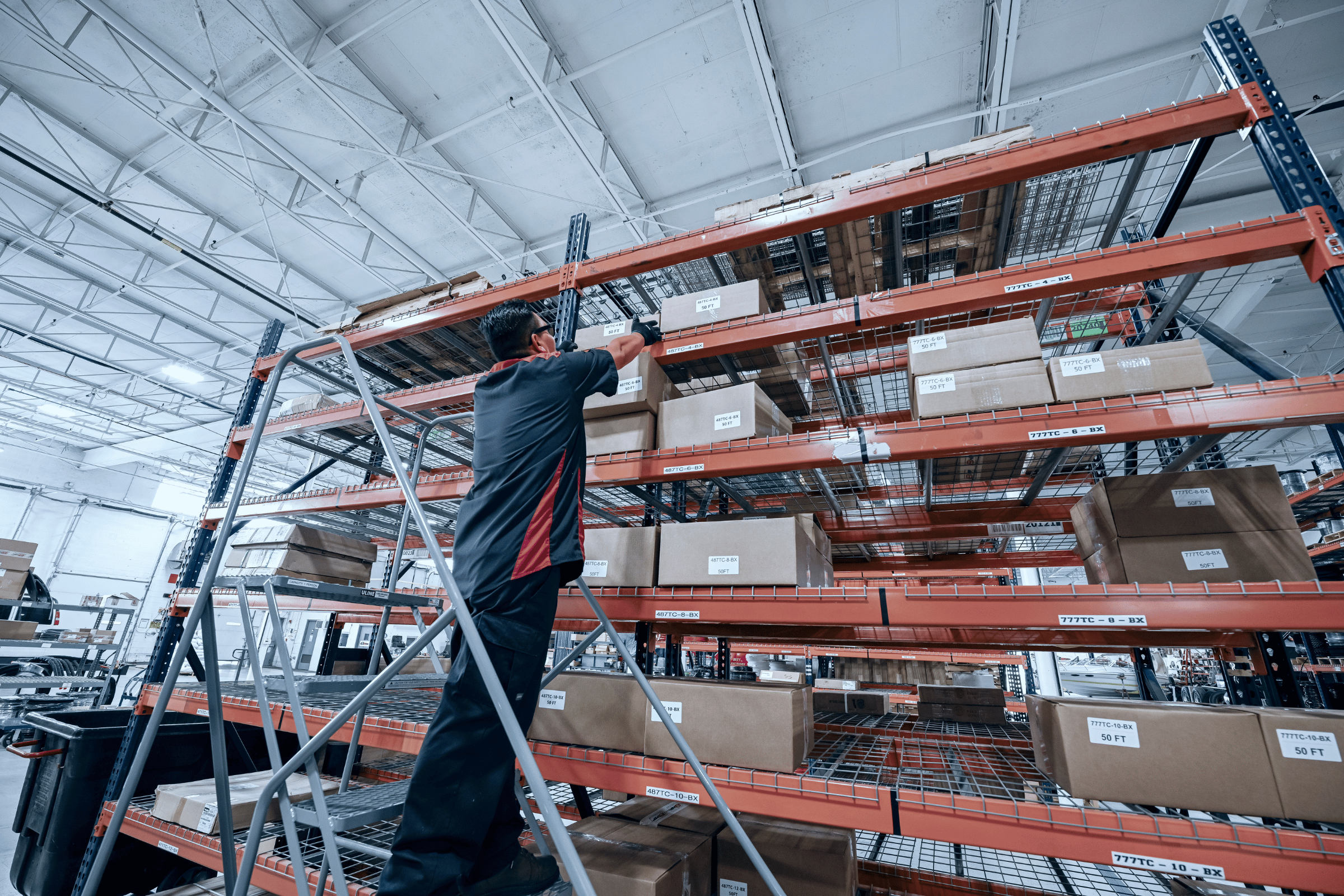 employee on scaffolding reaching for a box on rack shelving