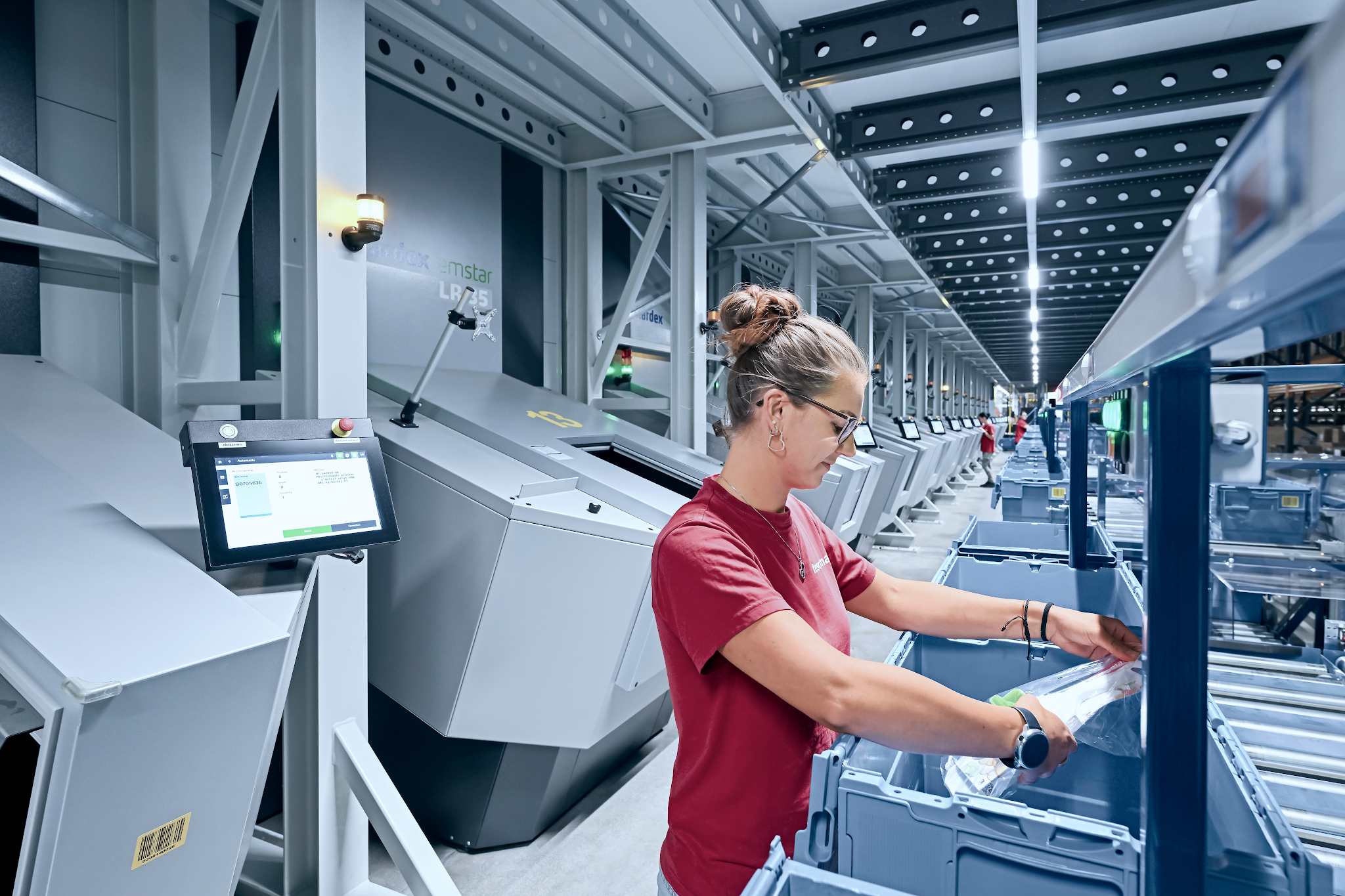 Operaria realizando picking automatizado en una estación de trabajo ergonómica integrada con un módulo de almacenamiento vertical Kardex Remstar LR35.